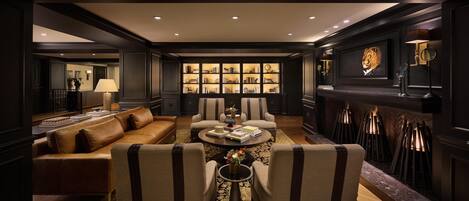 A luxurious living room with a dark wood paneling, a fireplace, a bookshelf, and a comfortable seating area.