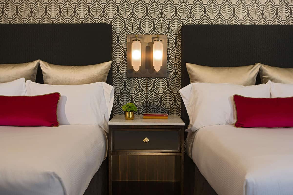 Een hotelkamer met twee bedden, een nachtkastje en een wandlamp.