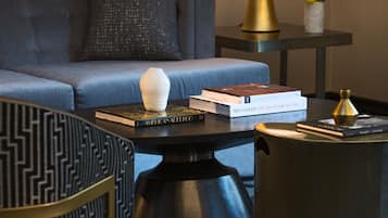 Una sala de estar moderna con un sofá, un sillón estampado, una mesa de centro con libros, una lámpara y un florero con flores.