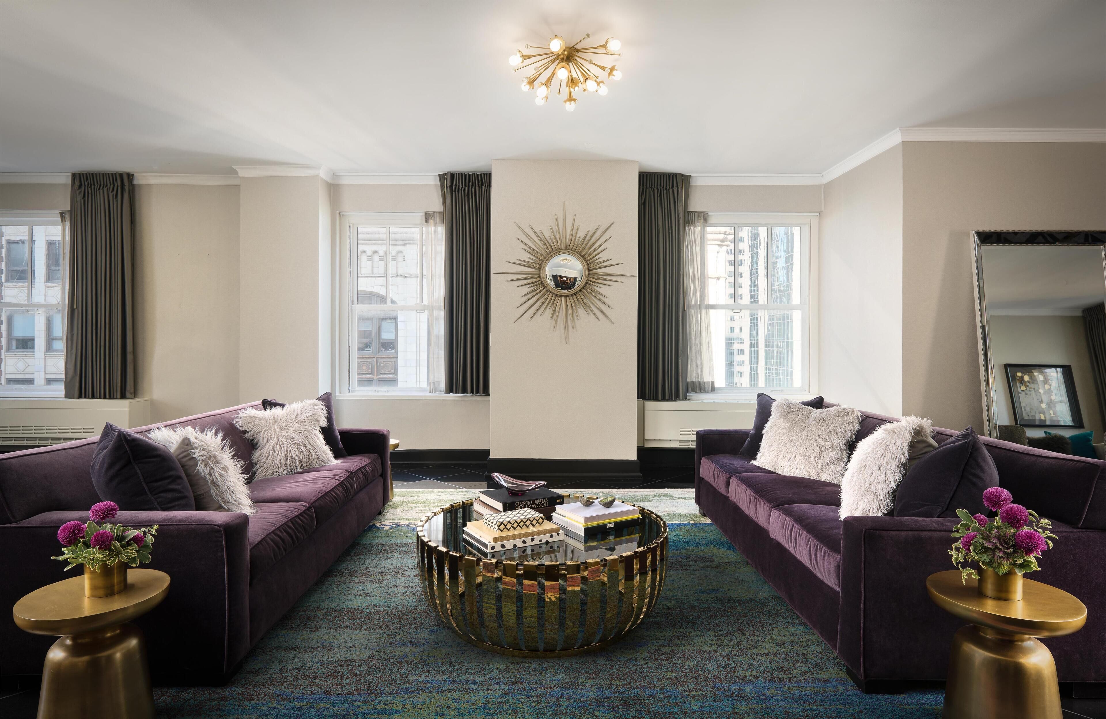 A modern living room with two purple sofas, a round coffee table, and a large mirror on the wall.