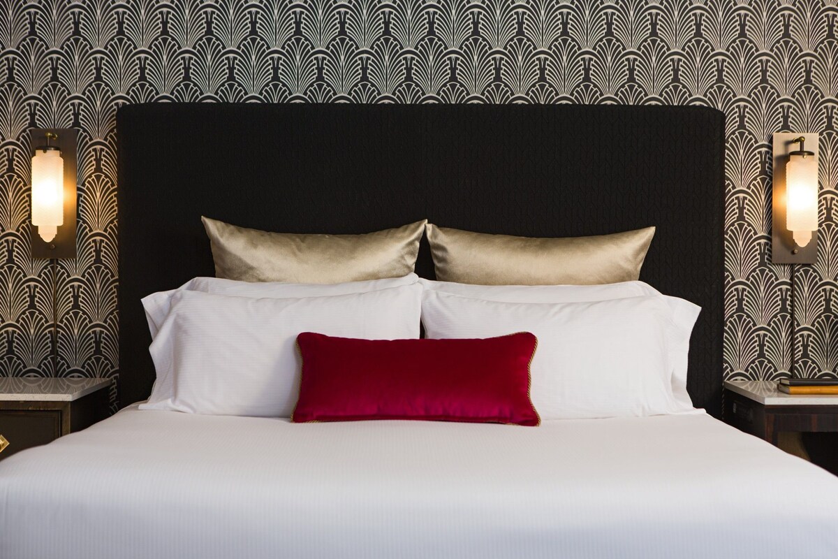A bed with white linens and two pillows, one red and one gold, against a patterned wallpaper.