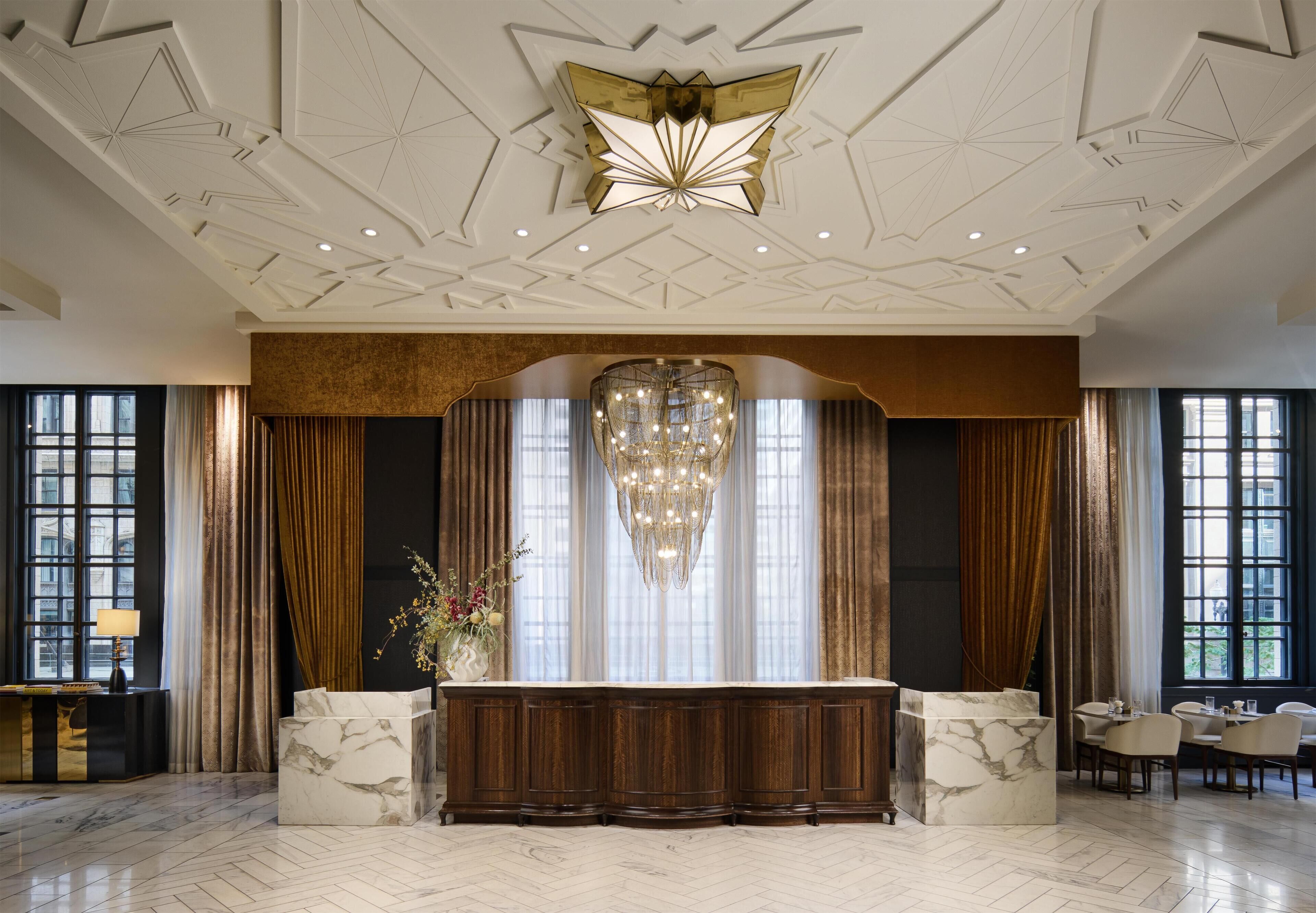 A lobby with a marble reception desk, a chandelier, and large windows with curtains.