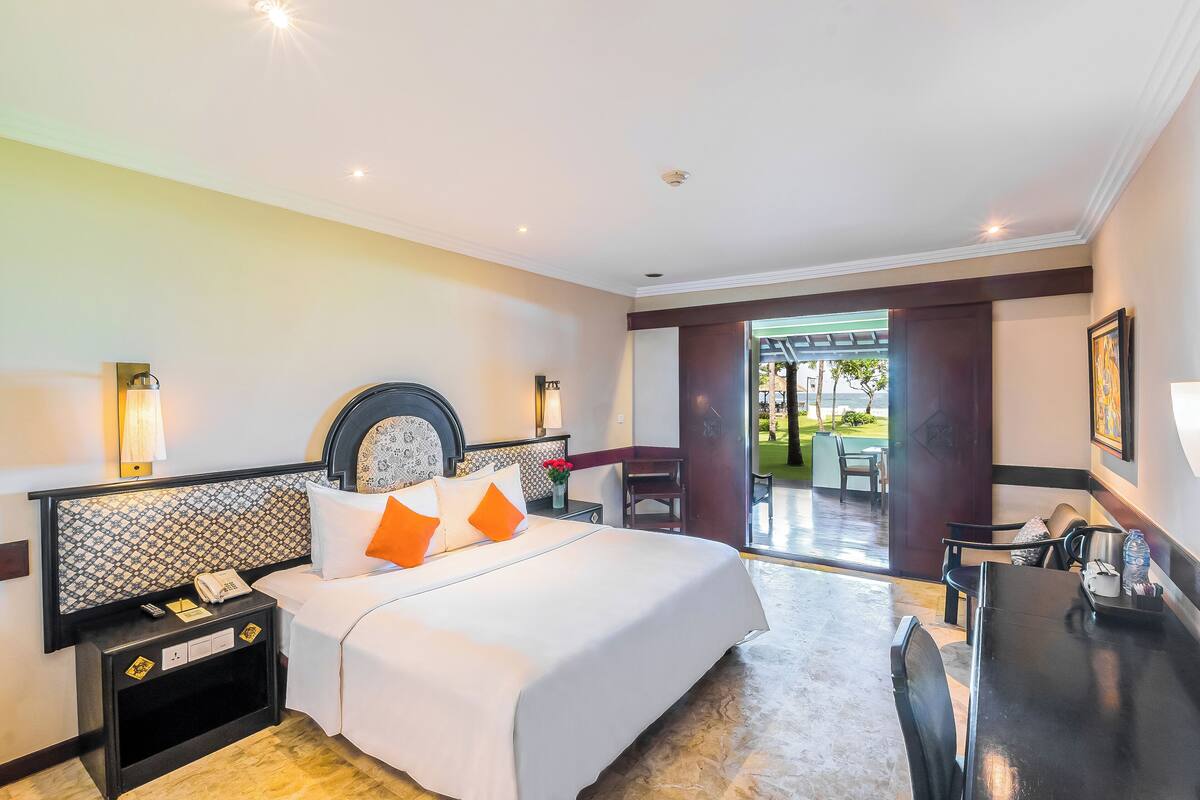 Ein Hotelzimmer mit Bett, Nachttisch, Lampe und Blick ins Freie.