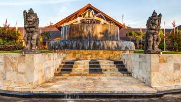 Una fuente de piedra con cascada, flanqueada por dos estatuas, frente a un edificio con un cartel que dice "DISCOVERY".