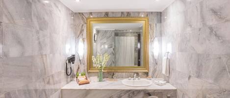 Un baño con paredes de mármol, un espejo con marco dorado, un lavabo y una zona de ducha.