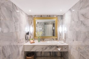 A bathroom with marble walls, a gold-framed mirror, a sink, and a shower area.