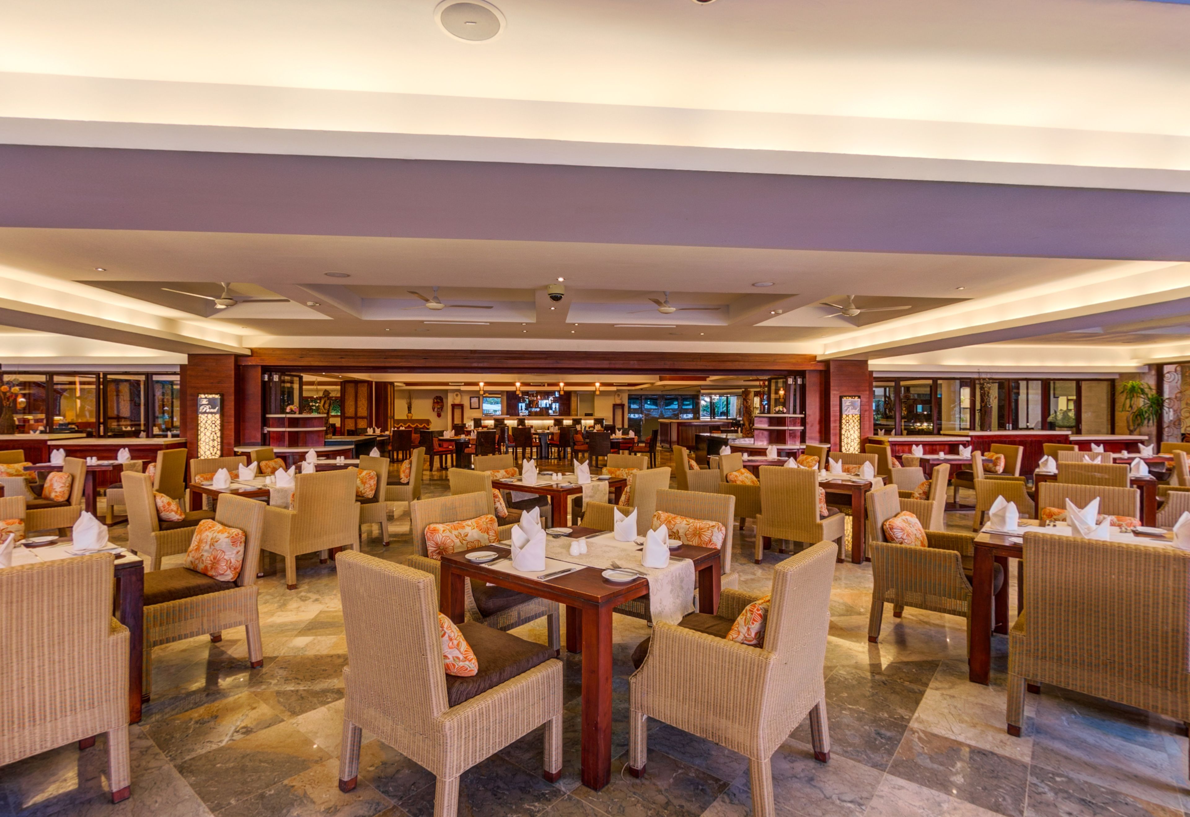 A spacious restaurant with multiple dining areas, each featuring tables and chairs, and a bar area in the background.