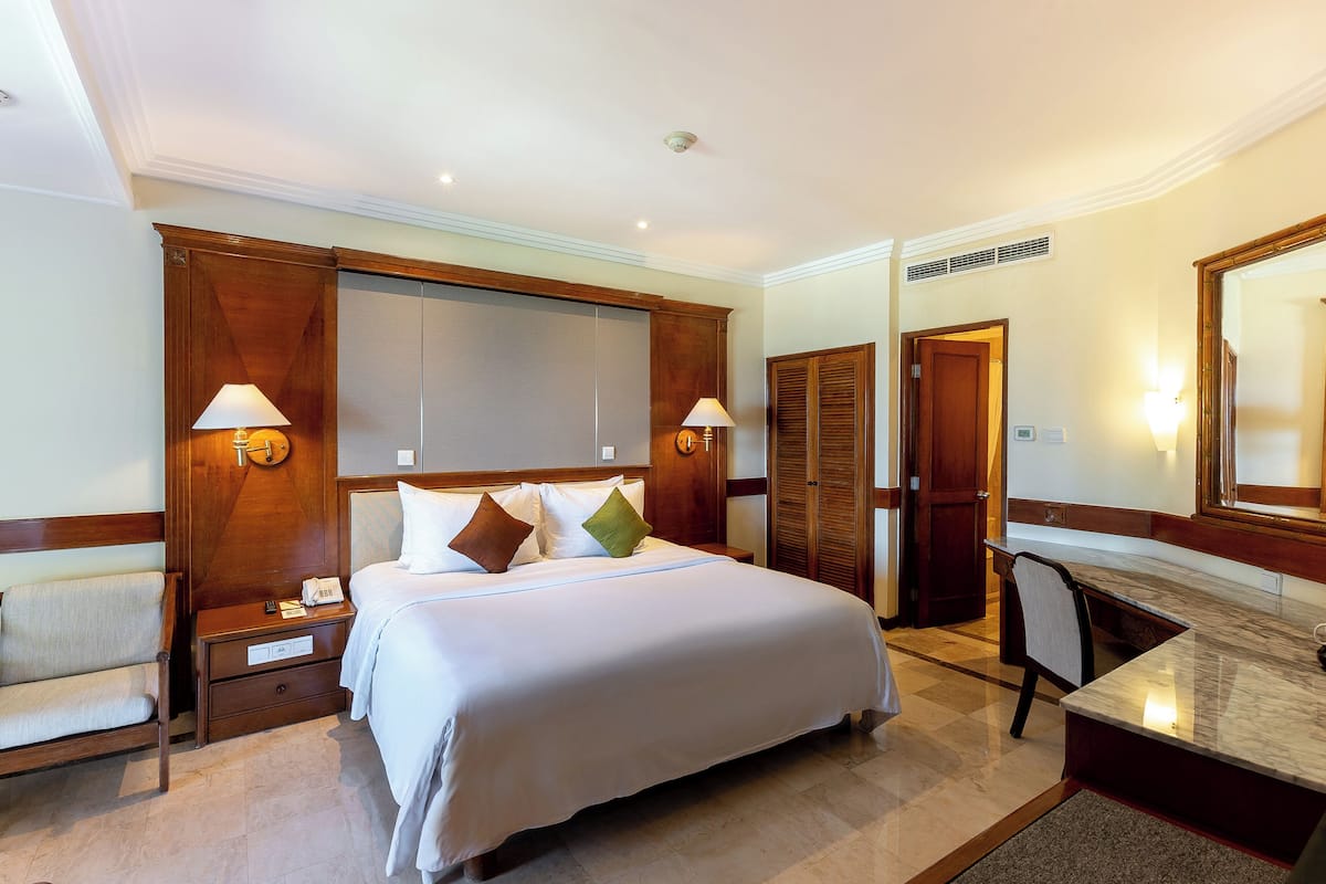 Ein Hotelzimmer mit einem großen Bett, Nachttischen, einem Schreibtisch und einem Spiegel.