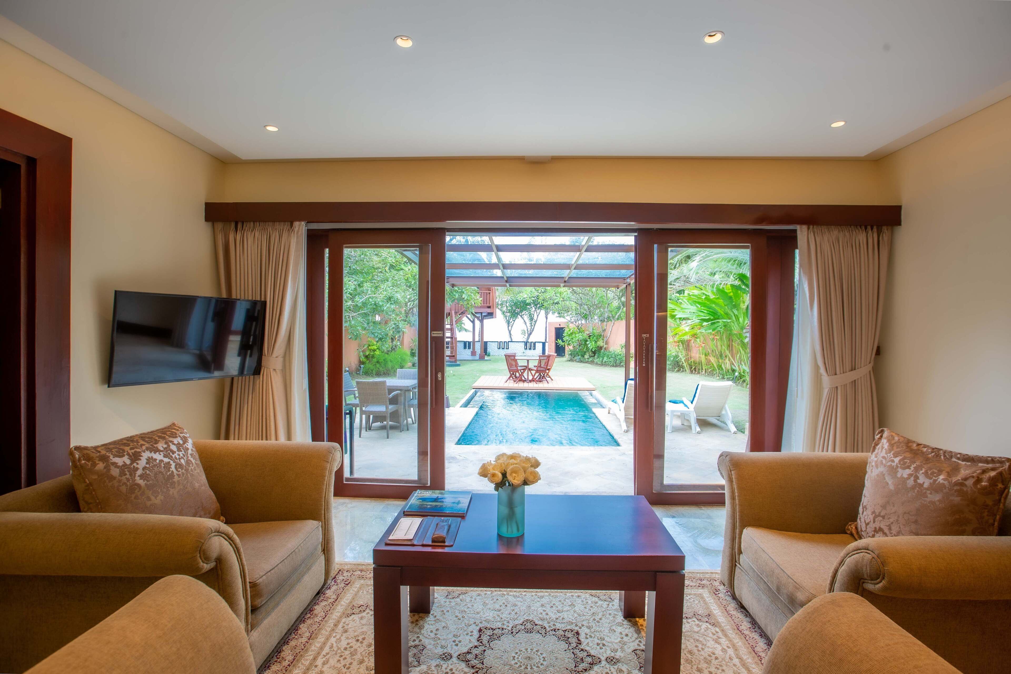 A living room with a sofa, a coffee table with a vase of flowers, and a flat-screen TV on the wall.