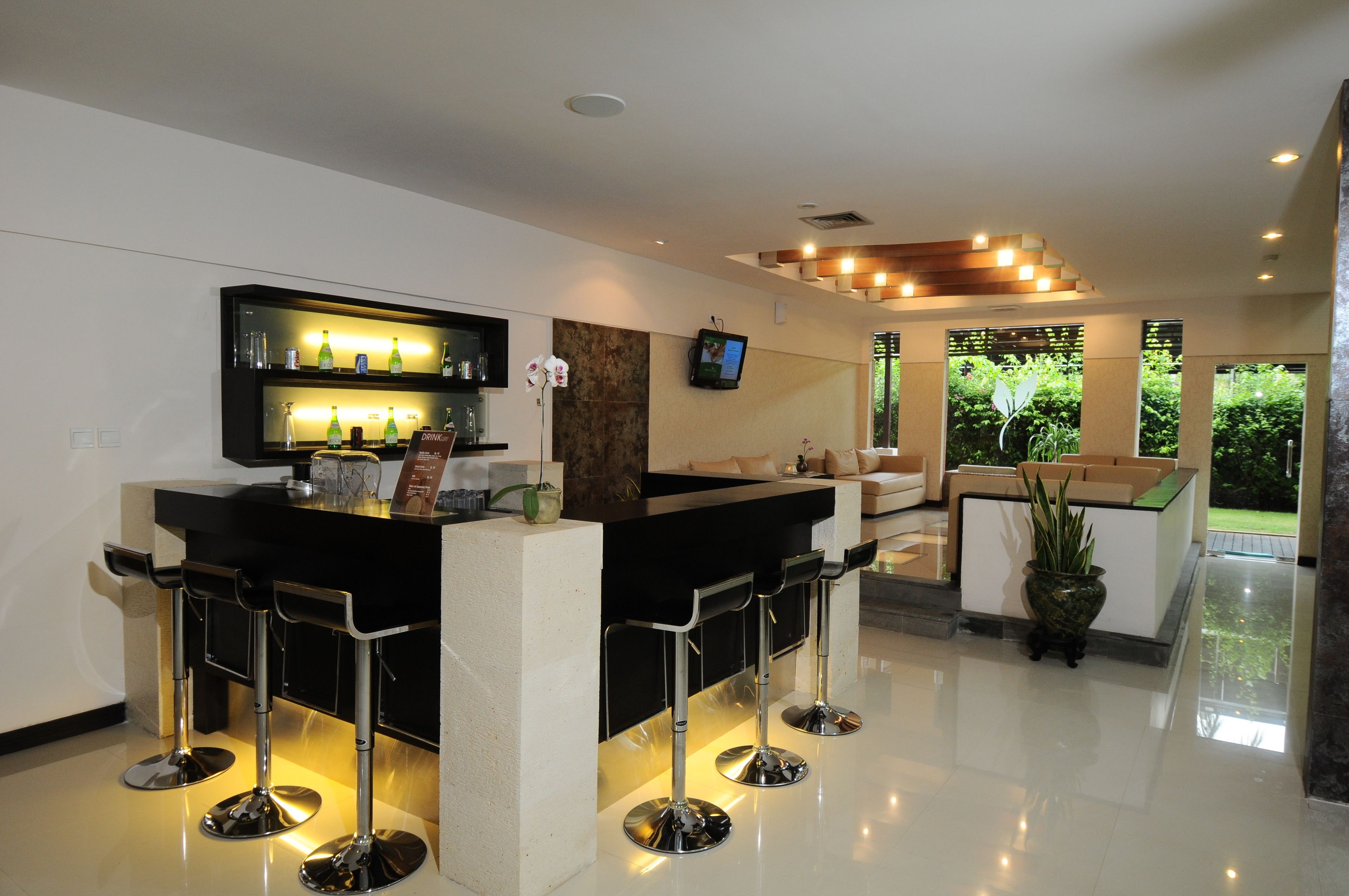 A modern bar area with a black countertop, three bar stools, and a television mounted on the wall.
