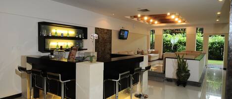 A modern bar area with a black countertop, three bar stools, and a television mounted on the wall.