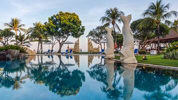 A clear swimming pool with blue water, surrounded by palm trees and lounge chairs.
