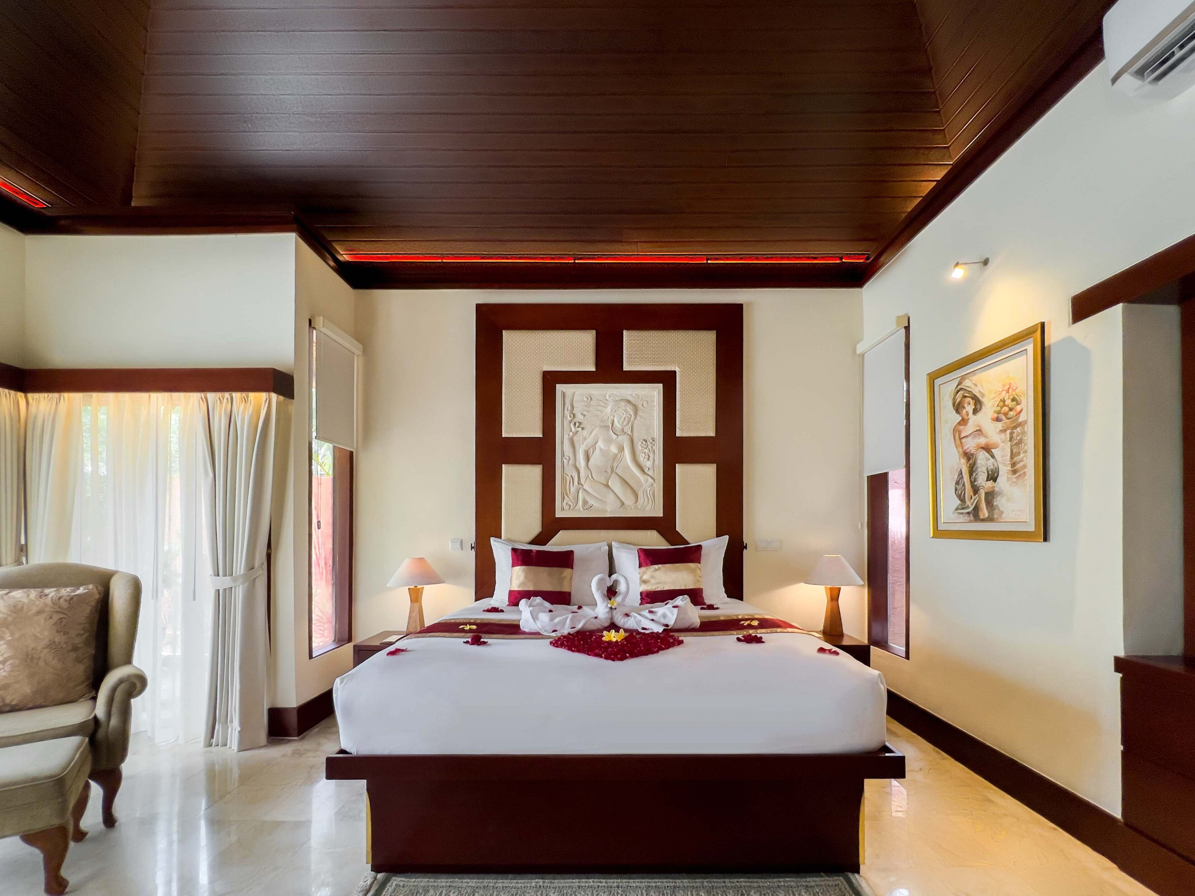 A hotel room with a large bed, a chair, a painting, and a decorative wall panel.