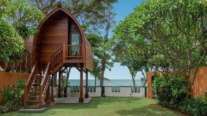 Una casa árbol de madera con balcón, rodeada de exuberante vegetación y vista al mar.