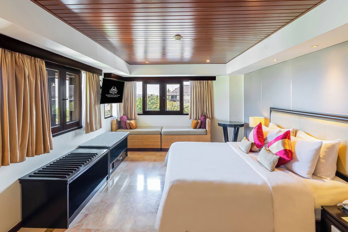 Ein Hotelzimmer mit Bett, Fernseher, einer Sitzecke und Blick auf Grünflächen.
