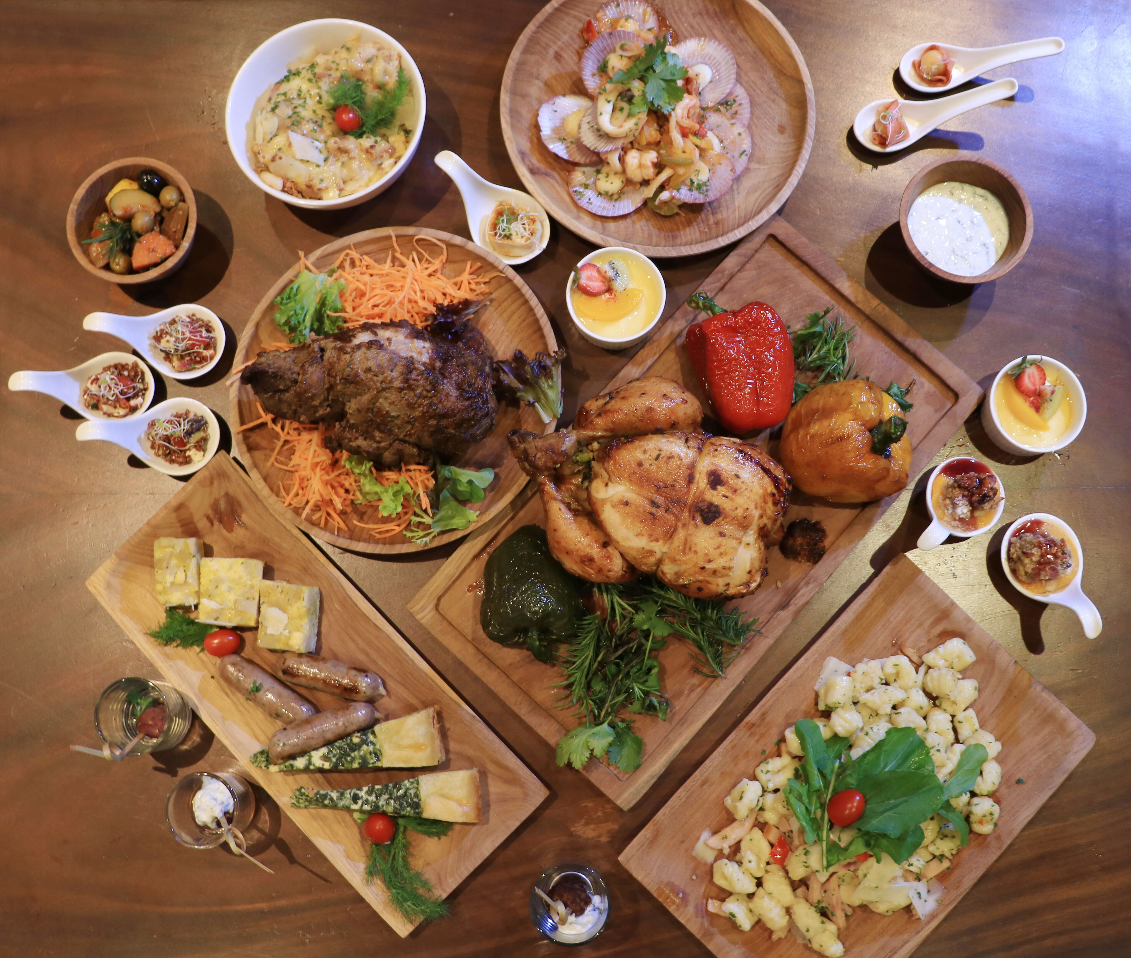 Variedad de platos que incluyen carnes asadas, verduras y pasta, dispuestos sobre una mesa de madera.
