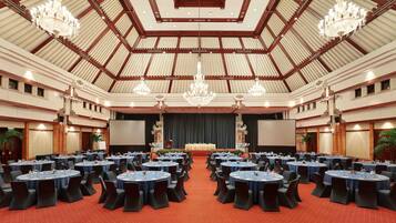 A large conference room with round tables and chairs, chandeliers, and a stage with a screen.