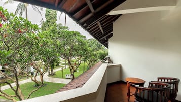A balcony with a view of a garden, a wooden table, and two chairs.