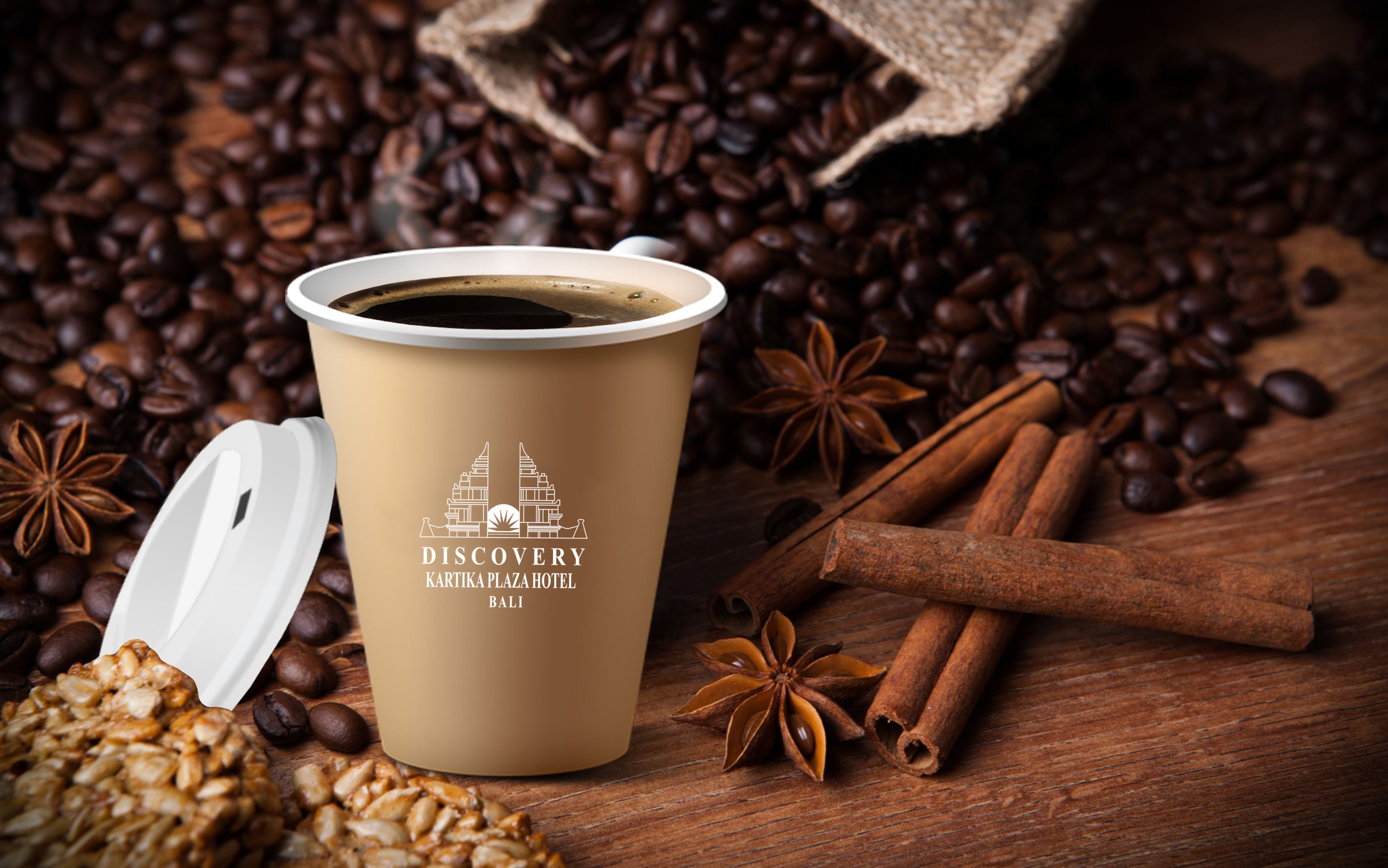Una taza de café con un logotipo y texto que indica que es del Kartika Plaza Hotel en Bali, rodeada de granos de café, ramas de canela y anís estrellado sobre una superficie de madera.