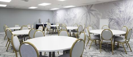 Une salle de conférence équipée de plusieurs tables rondes et de chaises, d’un tableau blanc et d’un distributeur d’eau.