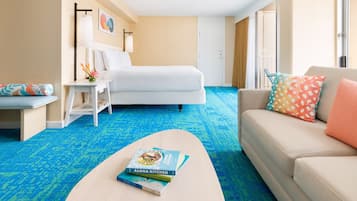 A hotel room with a bed, a sofa, a coffee table with a book, a nightstand, and a window with curtains.