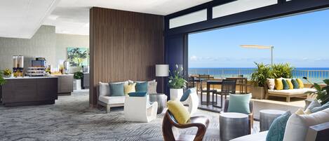 A modern hotel lobby with a large seating area, a reception desk, and a view of the ocean.