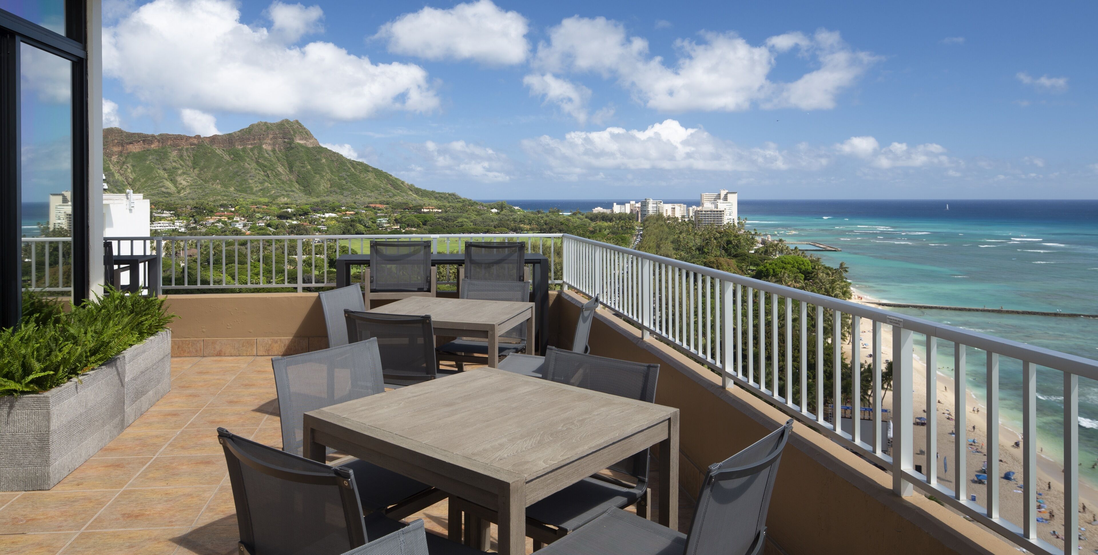A balcony with outdoor seating, overlooking a beach and ocean.
