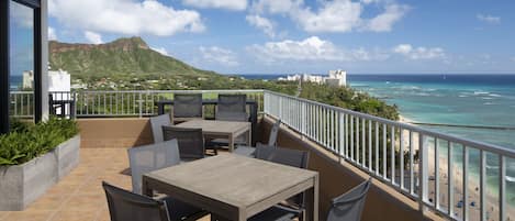 A balcony with outdoor seating, overlooking a beach and ocean.