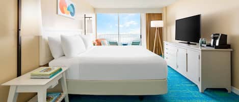 A hotel room with a large bed, a TV, a desk with books, and a view of the sky.