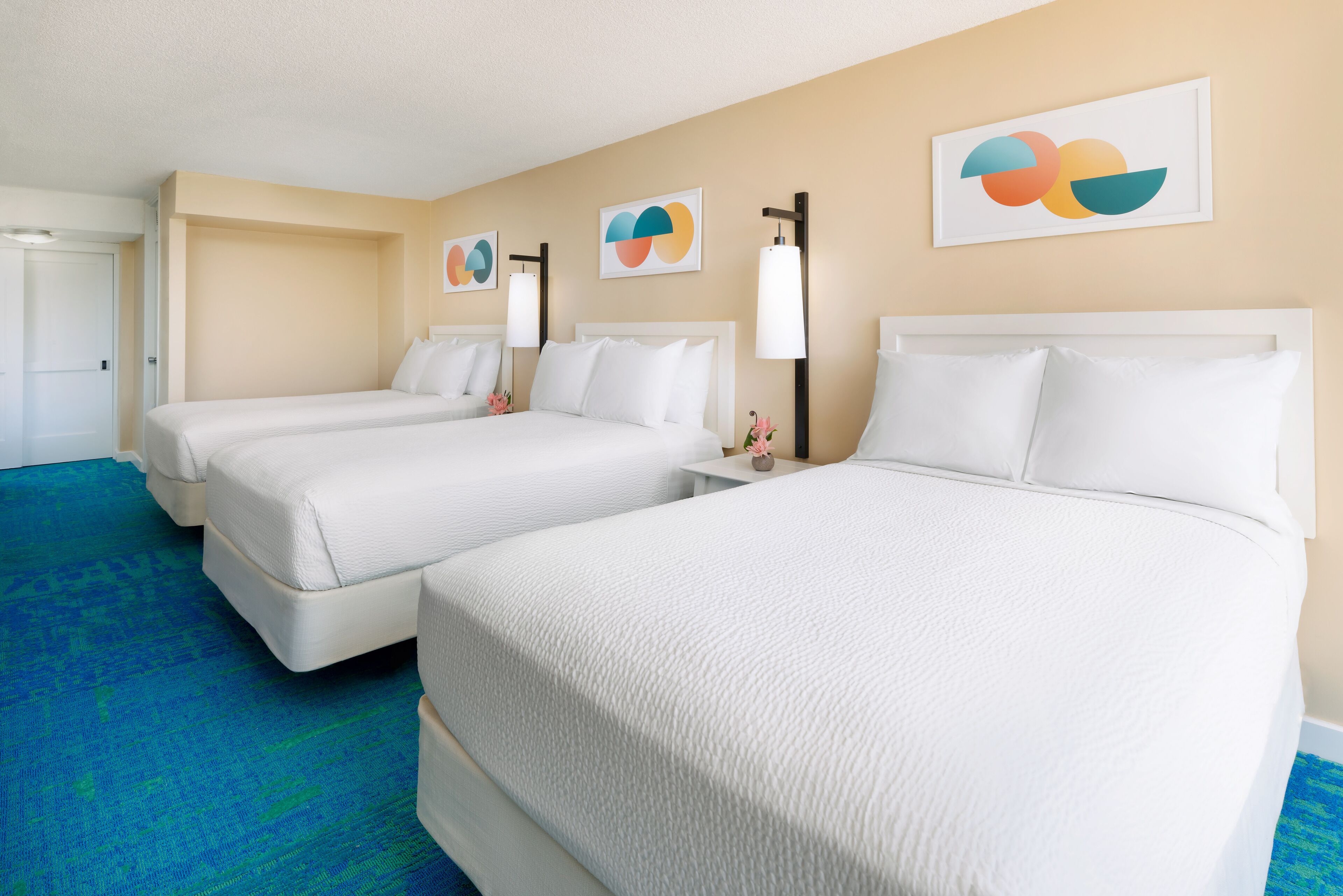 A hotel room with two beds, a blue carpet, and abstract wall art.