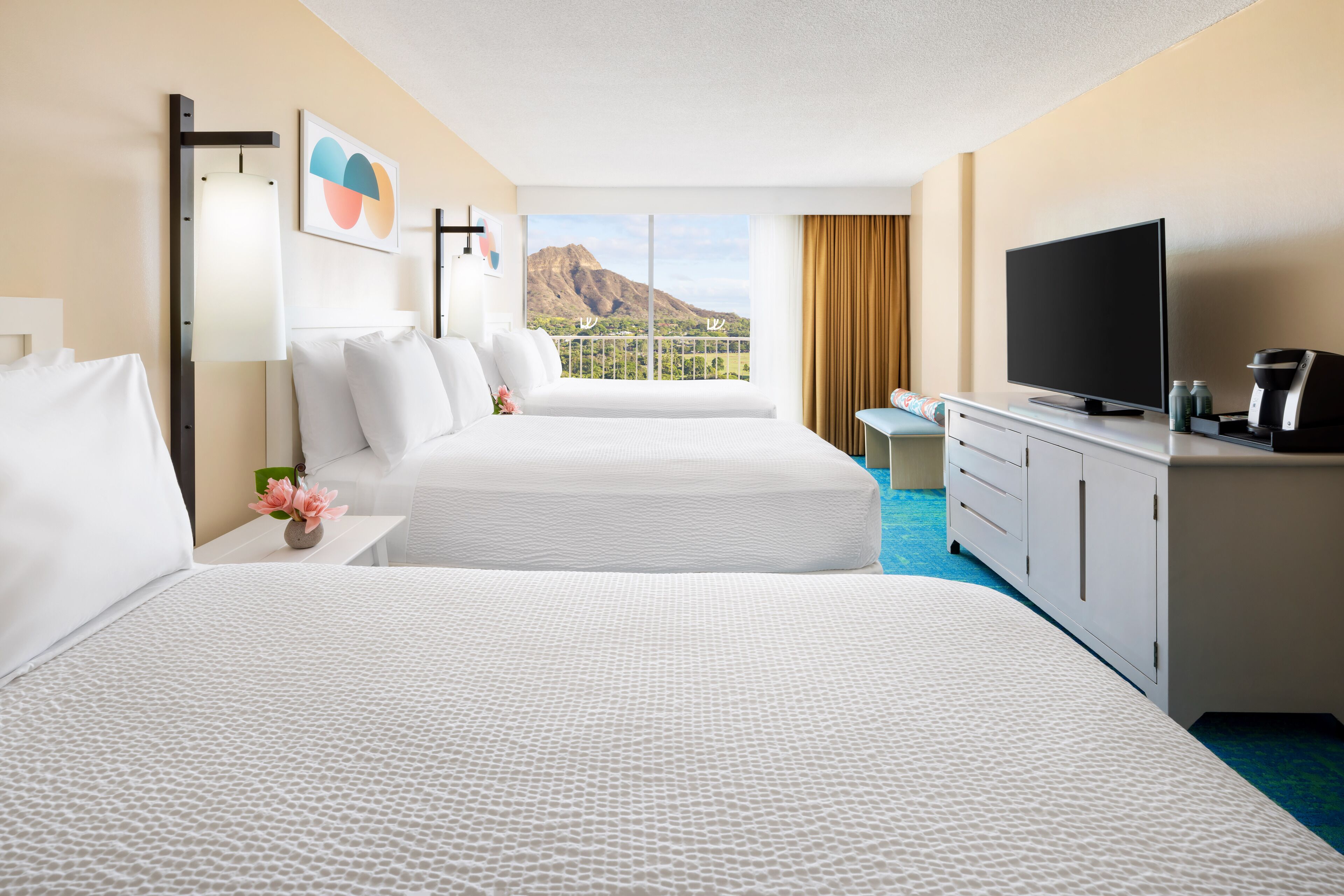 A hotel room with two beds, a TV, a desk, and a view of a mountain.