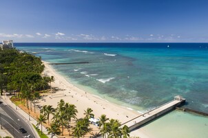 Una playa con agua turquesa cristalina, un muelle y palmeras.
