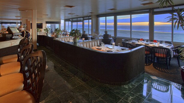 A spacious bar area with a curved counter, seating arrangements, and large windows offering a view of the ocean. - SeaVenture Beach Hotel (Pismo Beach)