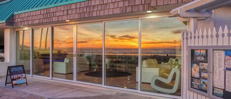 A coastal restaurant with large glass windows offering ocean views, outdoor seating, and a signboard advertising coastal cuisine.
