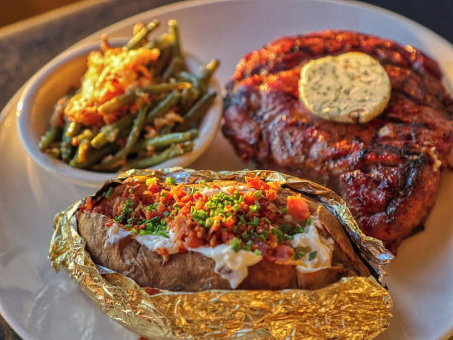 A plate with a grilled steak, baked potatoes, and green beans.