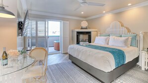 A bedroom with a bed, a ceiling fan, a fireplace, and a dining area with a table and chairs. - SeaVenture Beach Hotel (Pismo Beach)