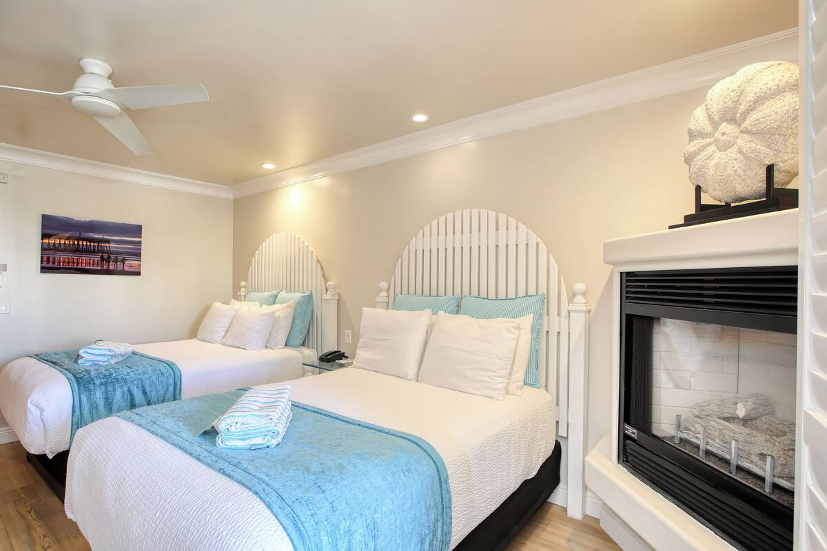 A hotel room with two beds, a fireplace, and a ceiling fan.