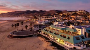A coastal town at dusk with a prominent hotel featuring a rooftop terrace and a view of the beach and mountains. - SeaVenture Beach Hotel (Pismo Beach)