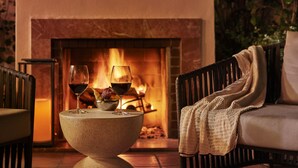 A cozy seating area with a fireplace, a table with glasses, and a chair with a blanket. - Hotel Bel-Air - Dorchester Collection (Los Angeles)