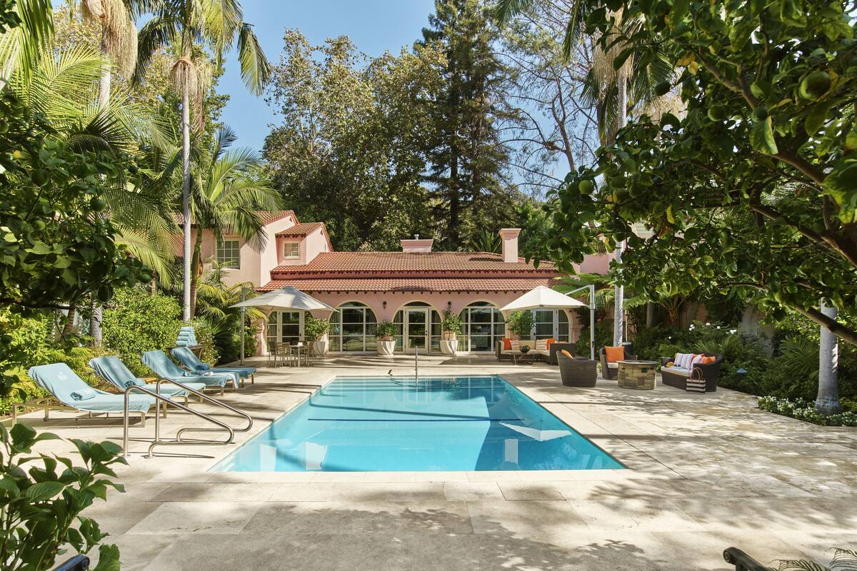 A swimming pool with lounge chairs, a covered seating area, and a building with a red-tiled roof.
