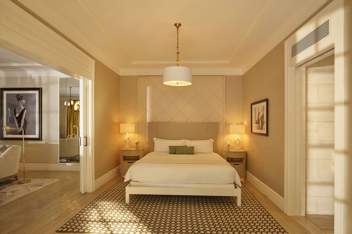 A hotel room with a large bed, two bedside tables with lamps, a mirror, a framed picture on the wall, and a patterned rug.