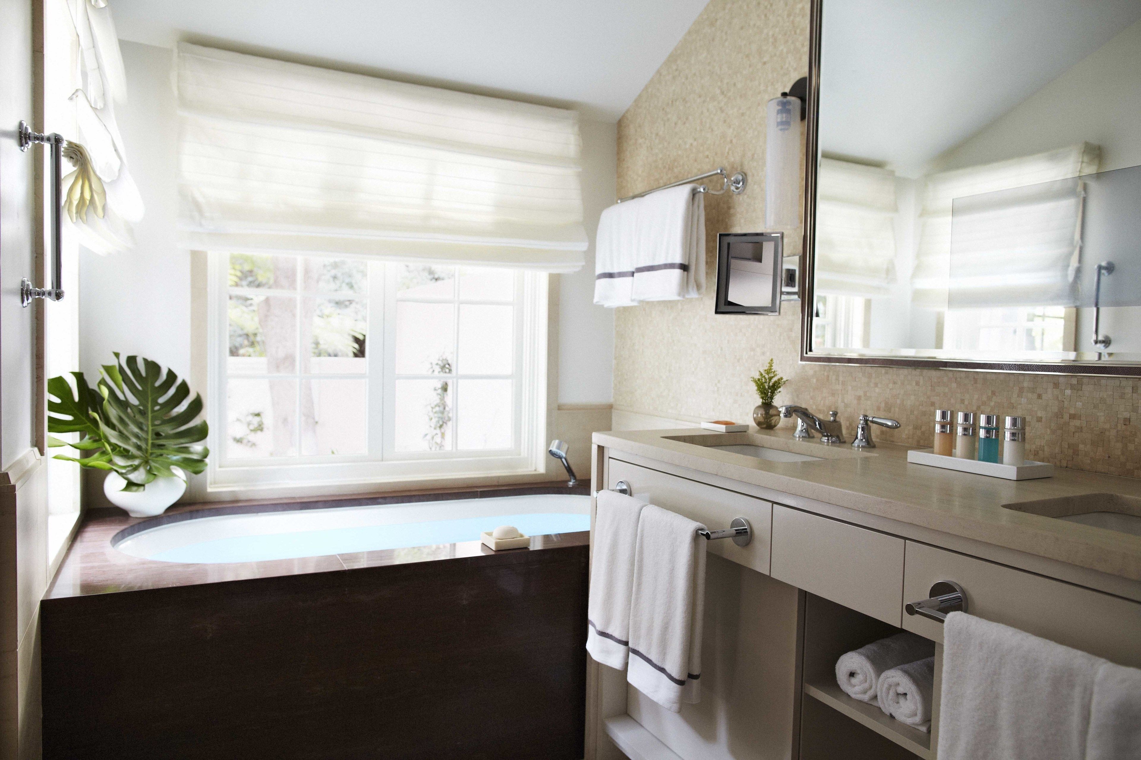 A modern bathroom with a large window, a bathtub, a sink, and a mirror.
