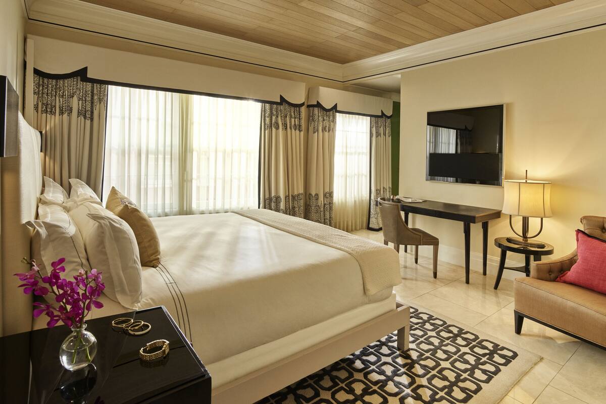 A hotel room with a large bed, a desk, a chair, a TV, and a lamp.