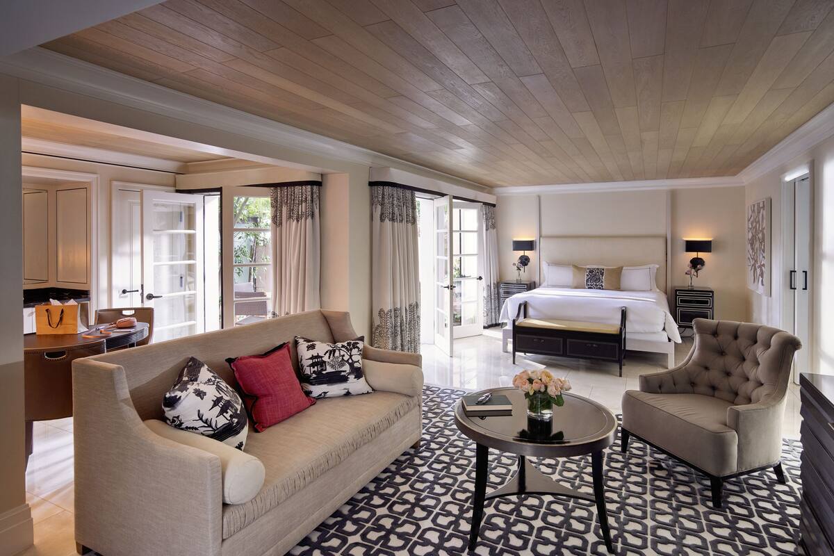 A spacious hotel room with a large bed, a sofa, a chair, and a dining area.