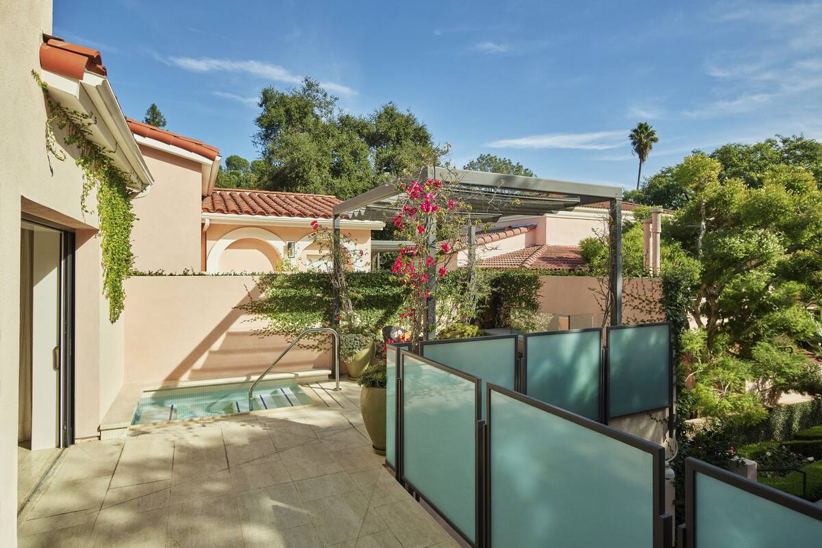 A pool area with a view of a building with a tiled roof and greenery.