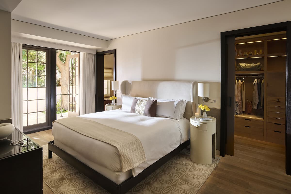 A modern hotel room with a large bed, bedside lamps, a wardrobe, and a view through a glass door.