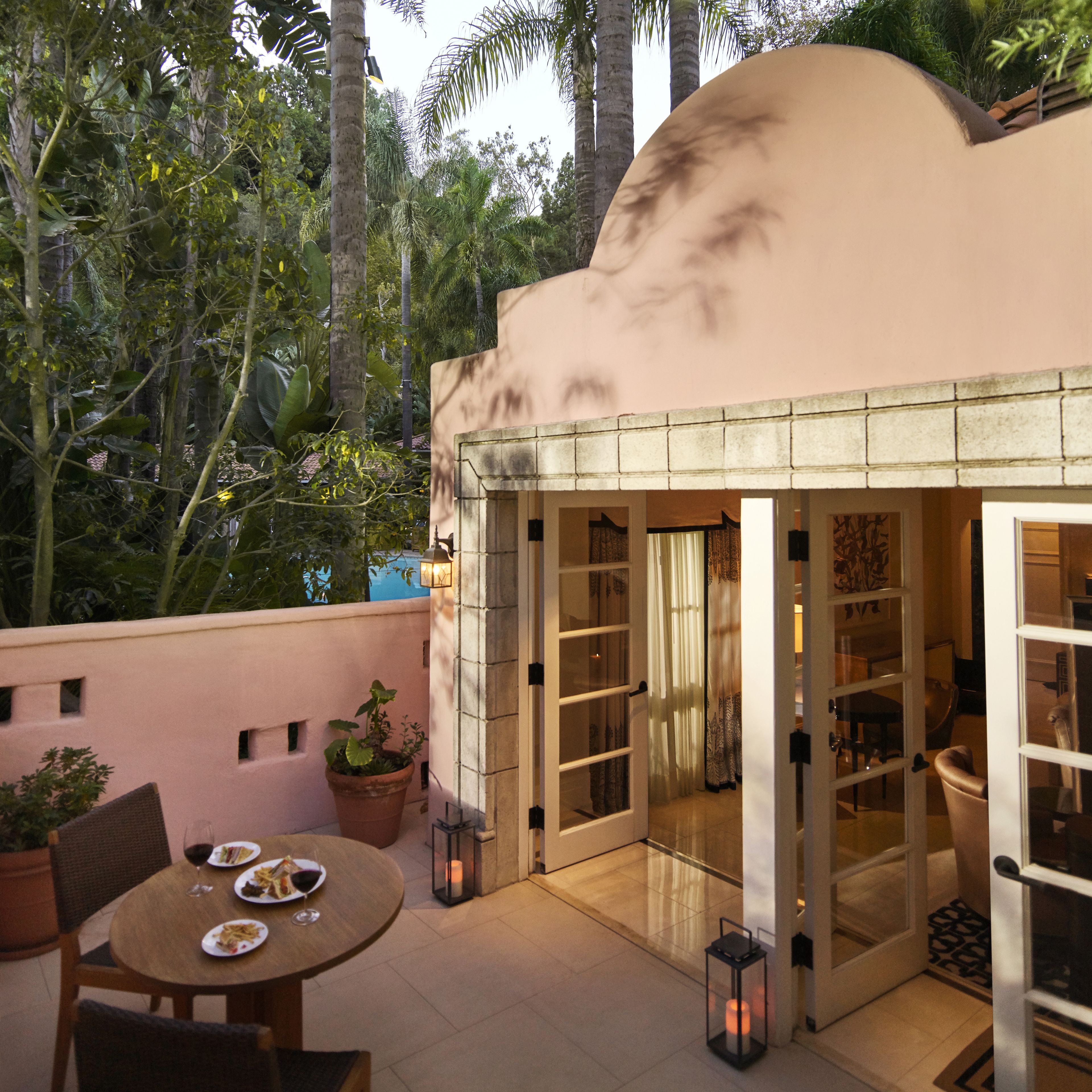 A patio with a table set for dining, surrounded by lush greenery and tall palm trees.