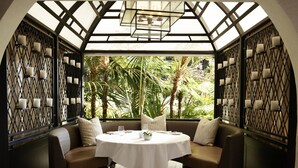 A cozy, enclosed dining area with a round table, two cushioned seating, and a view of lush greenery outside. - Hotel Bel-Air - Dorchester Collection (Los Angeles)