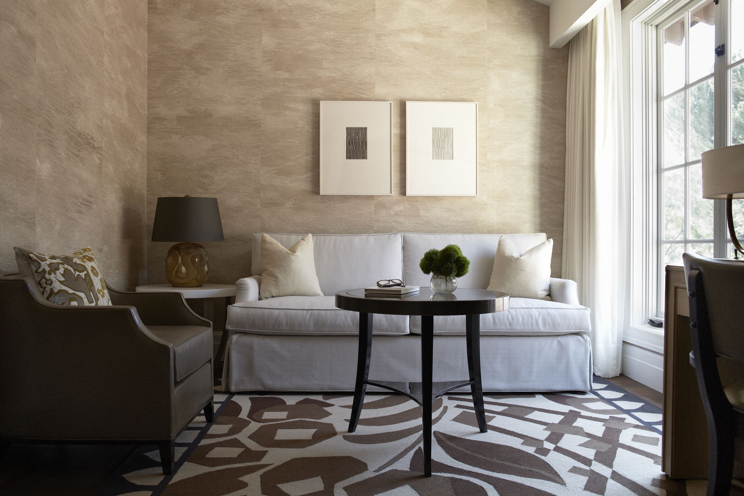 Una sala de estar moderna con una pared beige con textura, un sofá blanco, una mesa de centro negra redonda y una alfombra estampada.