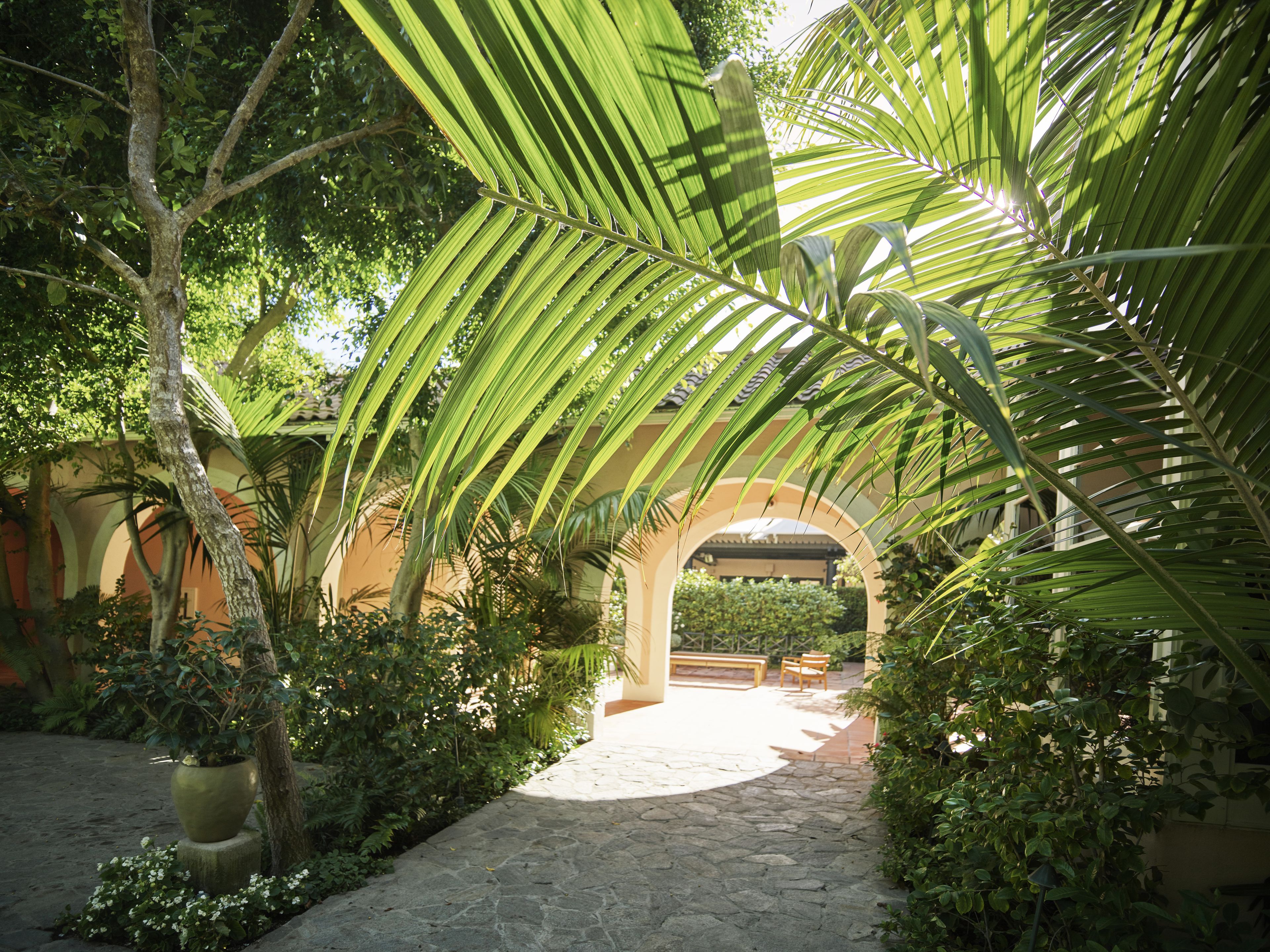 Un chemin de pierre traverse un jardin luxuriant agrémenté d’une pergola.